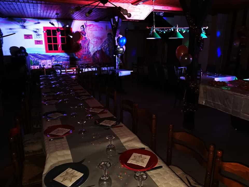 Une longue table dressée pour un dîner festif sous des lumières colorées, avec fresque flamenco, ballons et décorations.